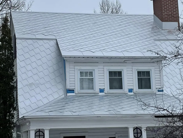 Maison blanche au toit gris enneigé et aux lucarnes, sous un ciel nuageux.