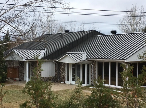 Maison avec un toit en métal noir et argent, des boiseries blanches et une façade en briques et en pierres.