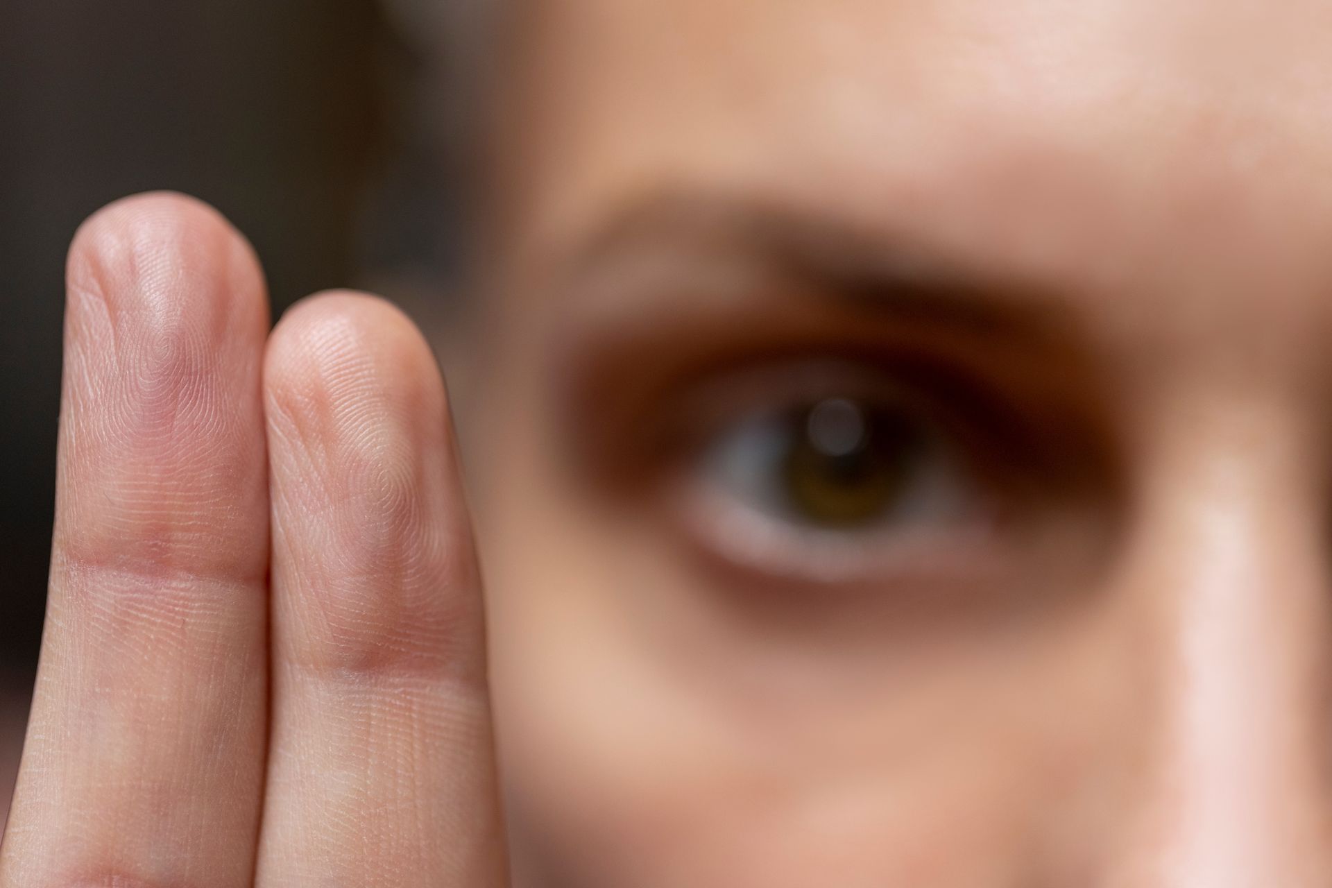 Two fingers held vertically in the foreground, slightly out of focus, with a person's eye visible in the blurred background.