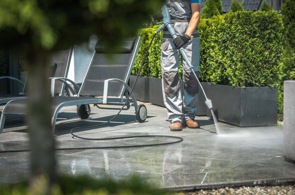 A man is using a high pressure washer to clean a patio — Pain in the Glass Window Cleaning in Proserpine, QLD