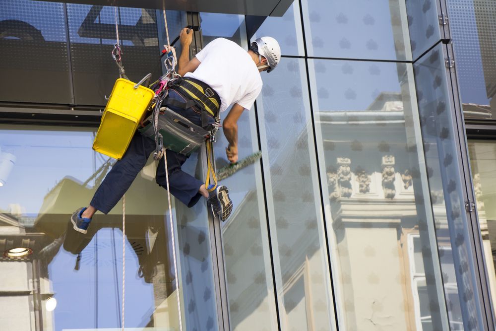 A person is cleaning a window with a high pressure washer — Pain in the Glass Window Cleaning in Proserpine, QLD