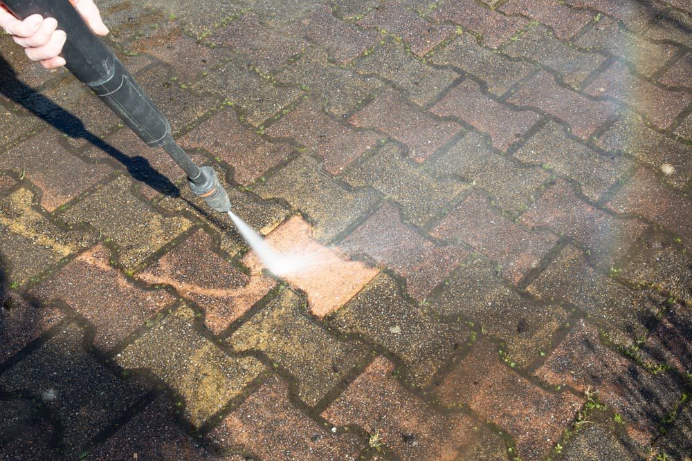 A person is using a high pressure washer to clean a brick walkway — Pain in the Glass Window Cleaning in Proserpine, QLD