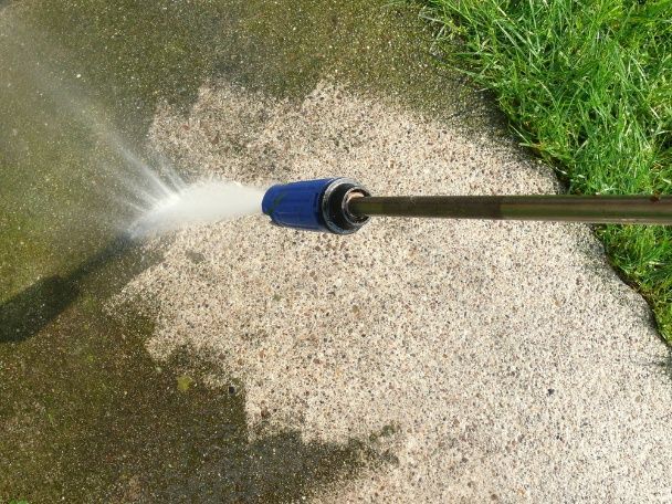 A Person is Using a High Pressure Washer to Clean a Sidewalk — Pain in the Glass Window Cleaning in Cannonvale, QLD