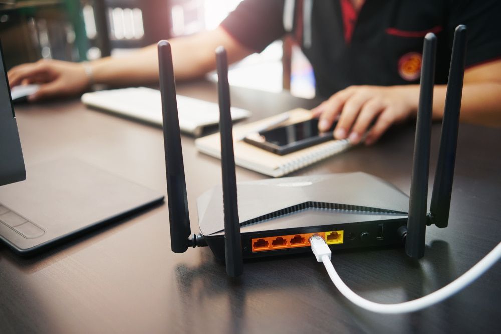 A Person Is Sitting At A Desk Using A Laptop And A Router — Comms Cabling Central Coast In Kanwal, NSW