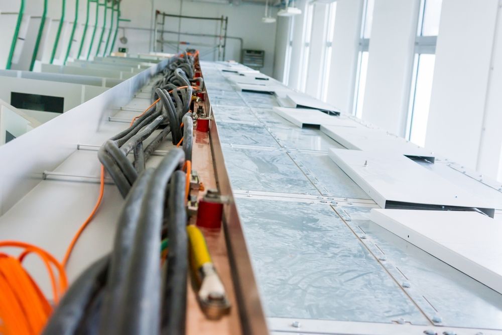 Electrical Cables and Conduit Running Along a Bright Industrial Floor Beside White Walls and Windows — Comms Cabling Central Coast In Kanwal, NSW