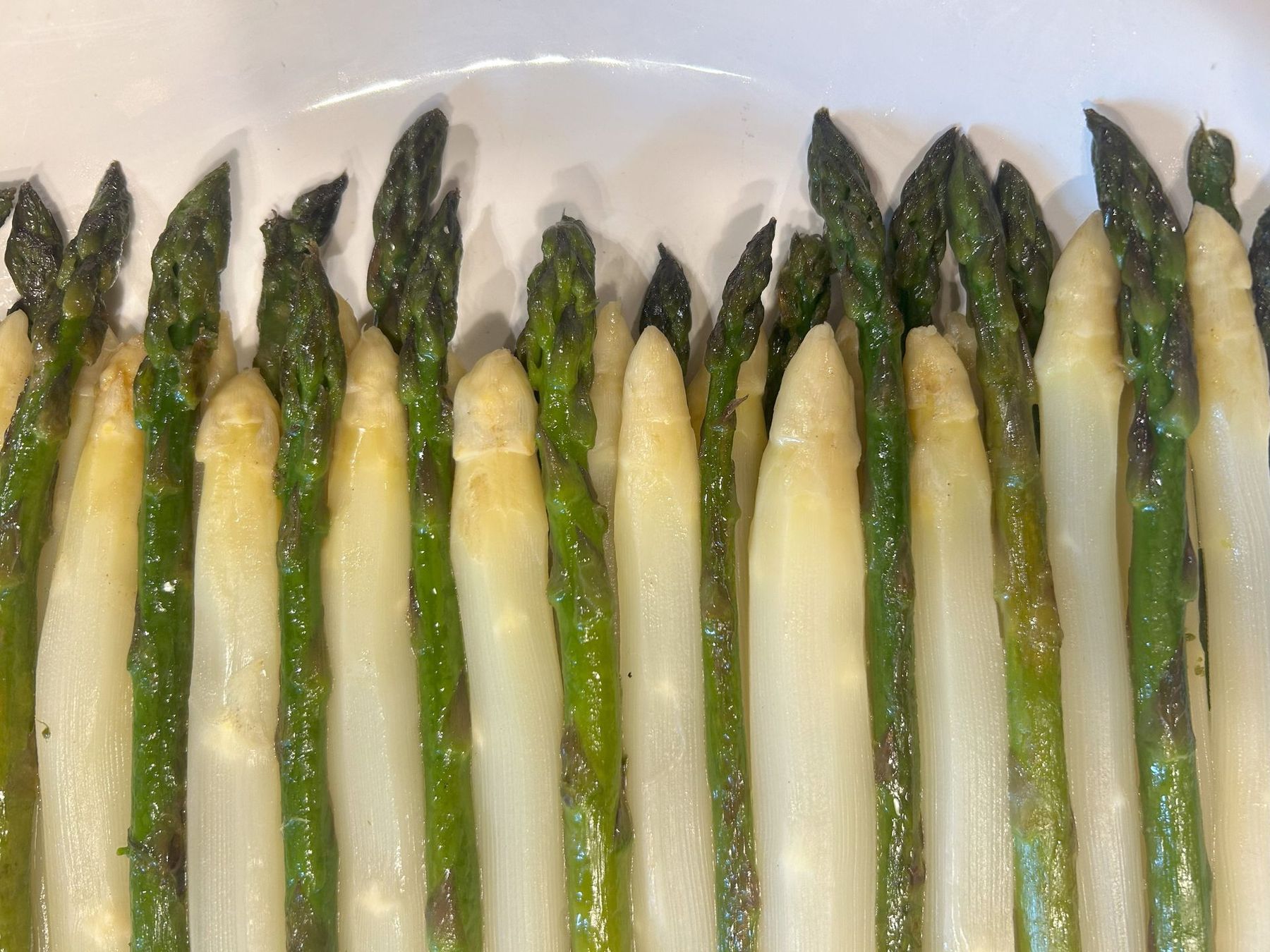 Fresh white asparagus spears arranged in a row on a white plate