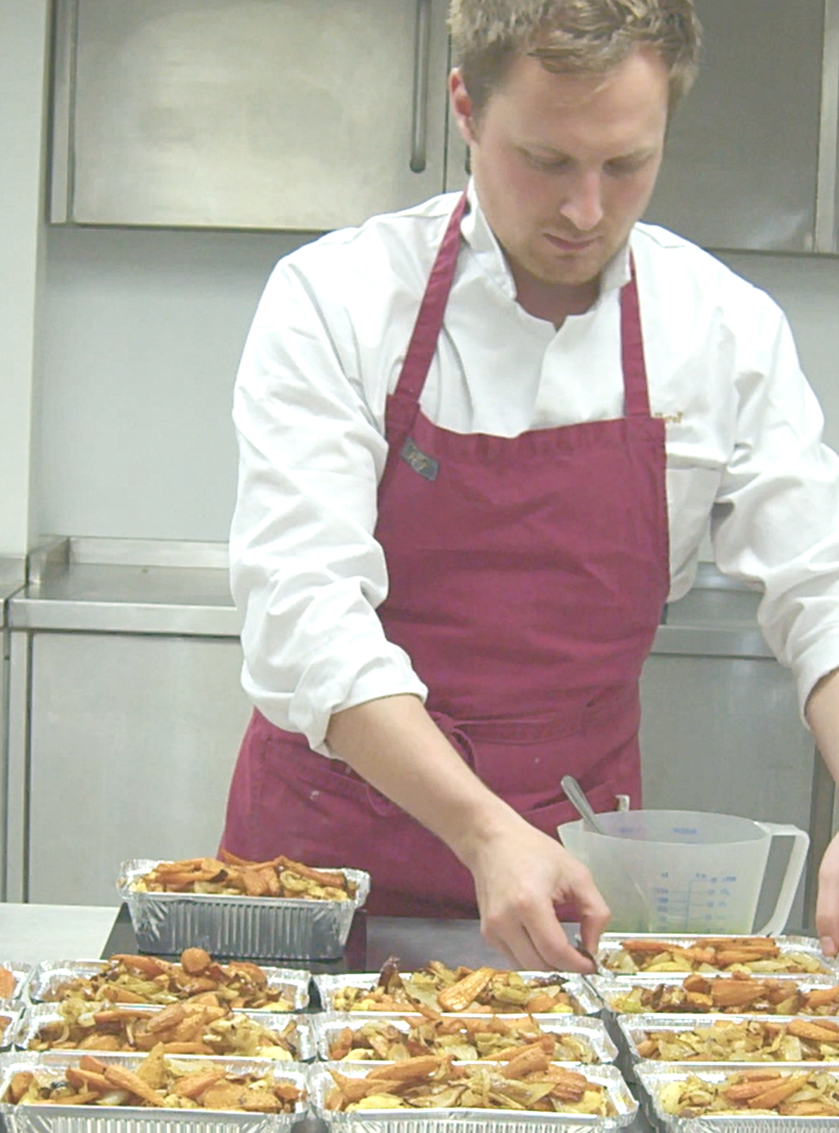 Chef in a red apron plating trays of food in a kitchen