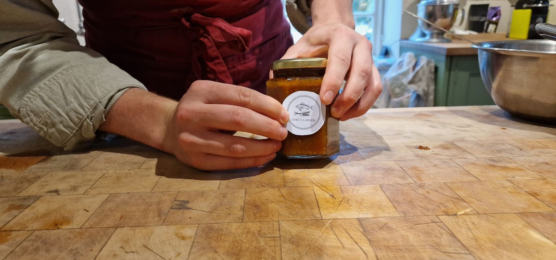 Hands labeling a small jar on a wooden counter in a kitchen workspace