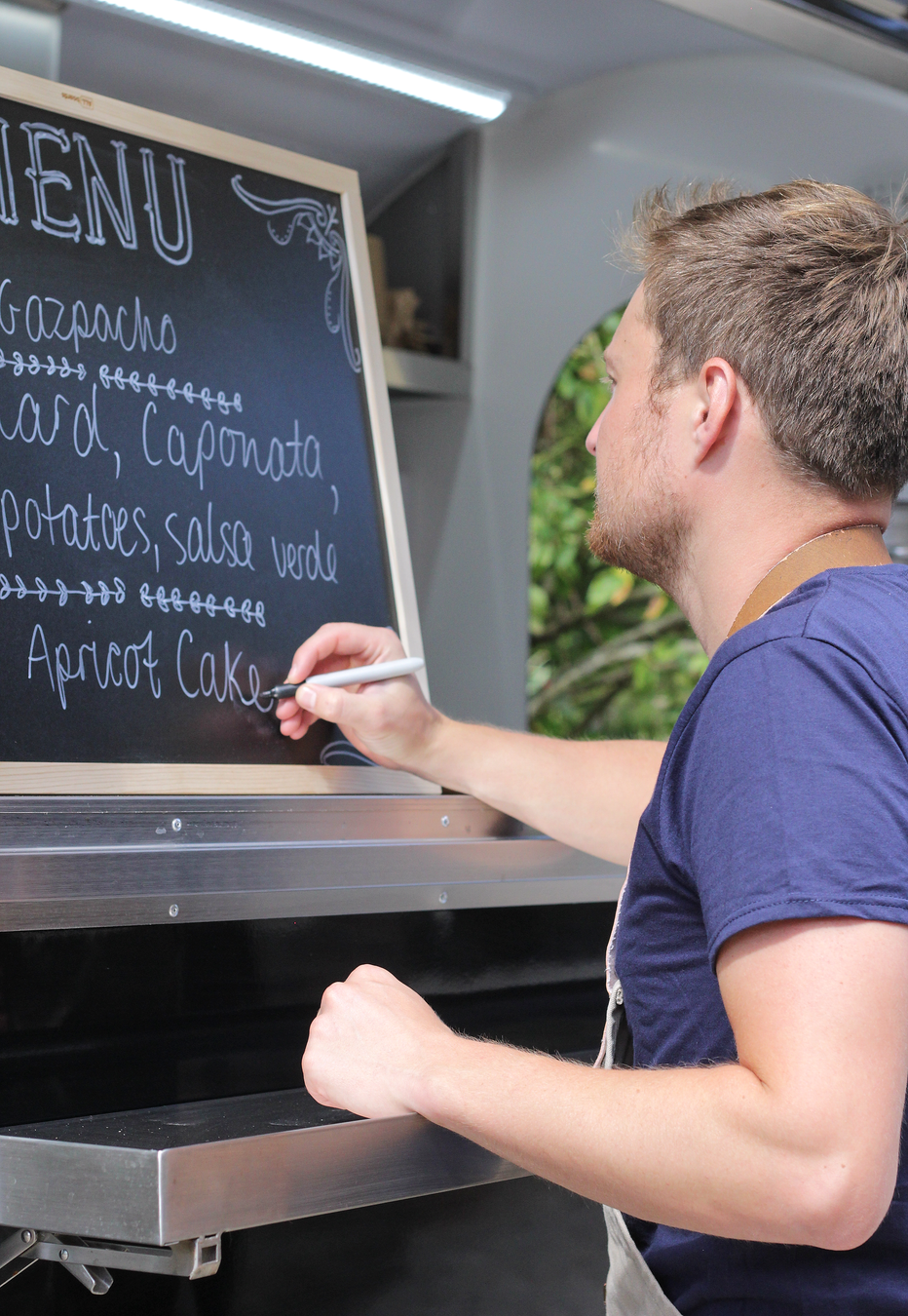 Man writing on a chalkboard menu inside a food truck window