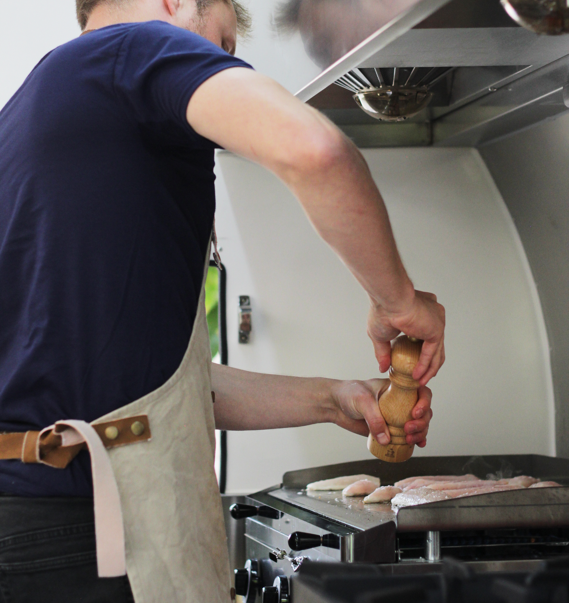 Person grilling meat while seasoning it with a pepper mill at an outdoor barbecue