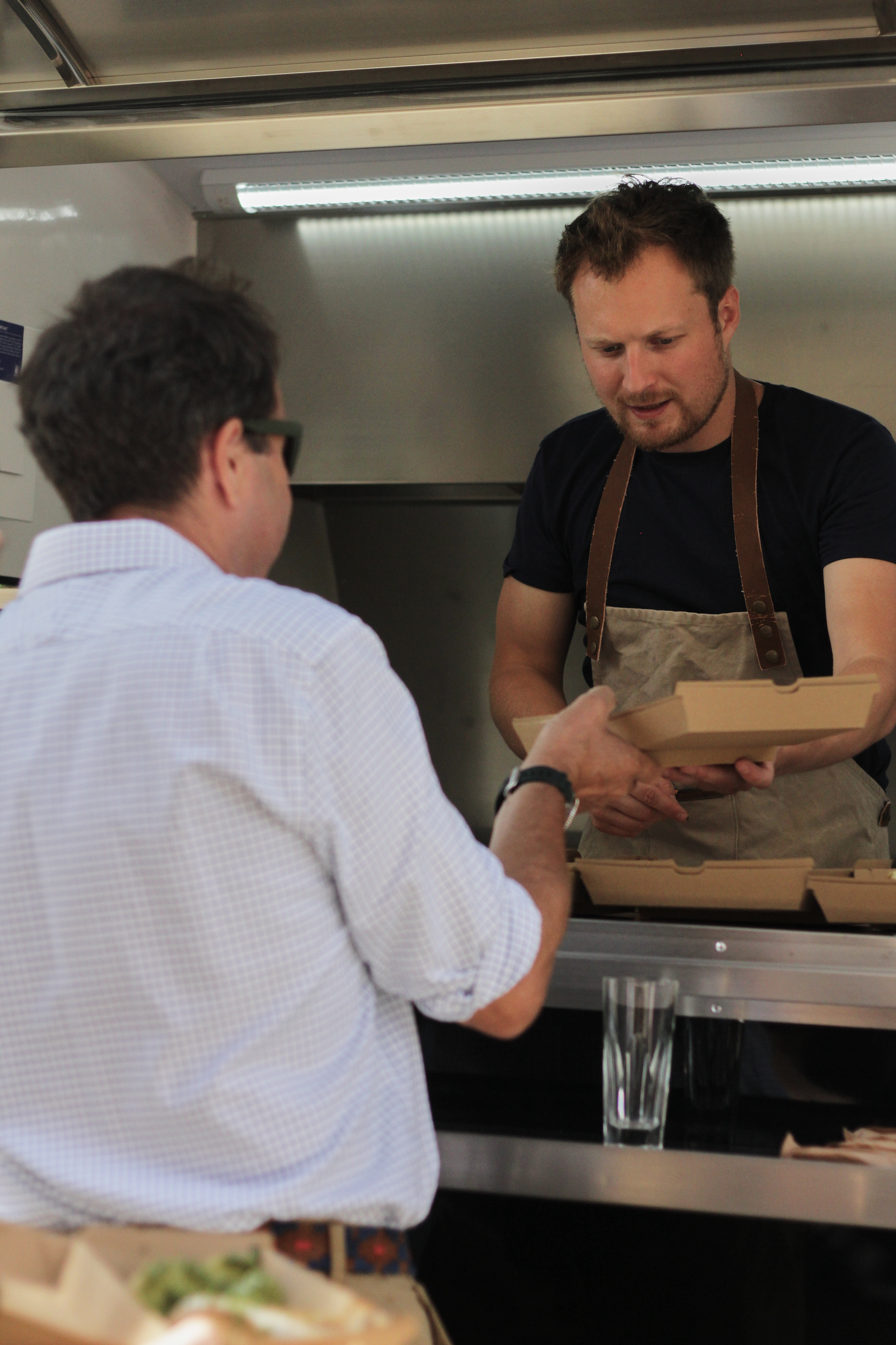 Two men exchanging a cardboard takeout box at a food truck counter.