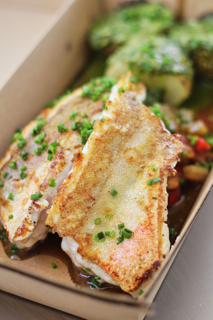 Takeout box with grilled fish fillets topped with chopped herbs