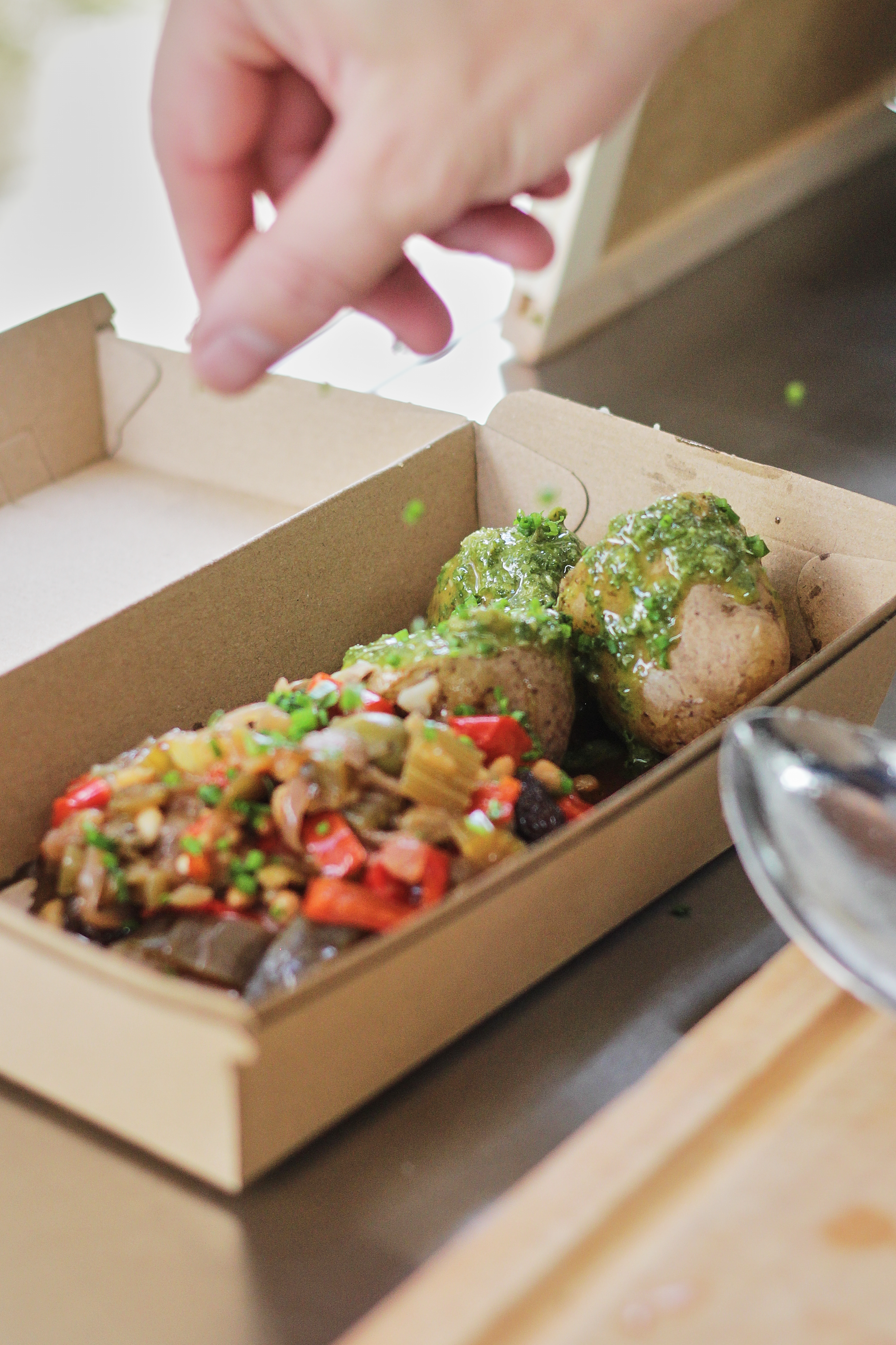 Hand placing sauced meatballs in a takeout box beside a colorful rice dish