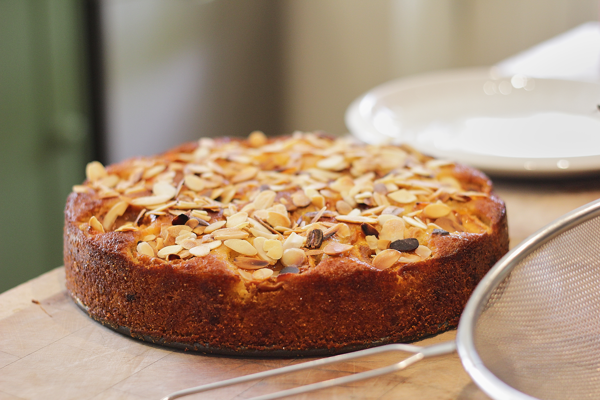 Round almond-topped cake on a tray with a powdered sugar sifter nearby