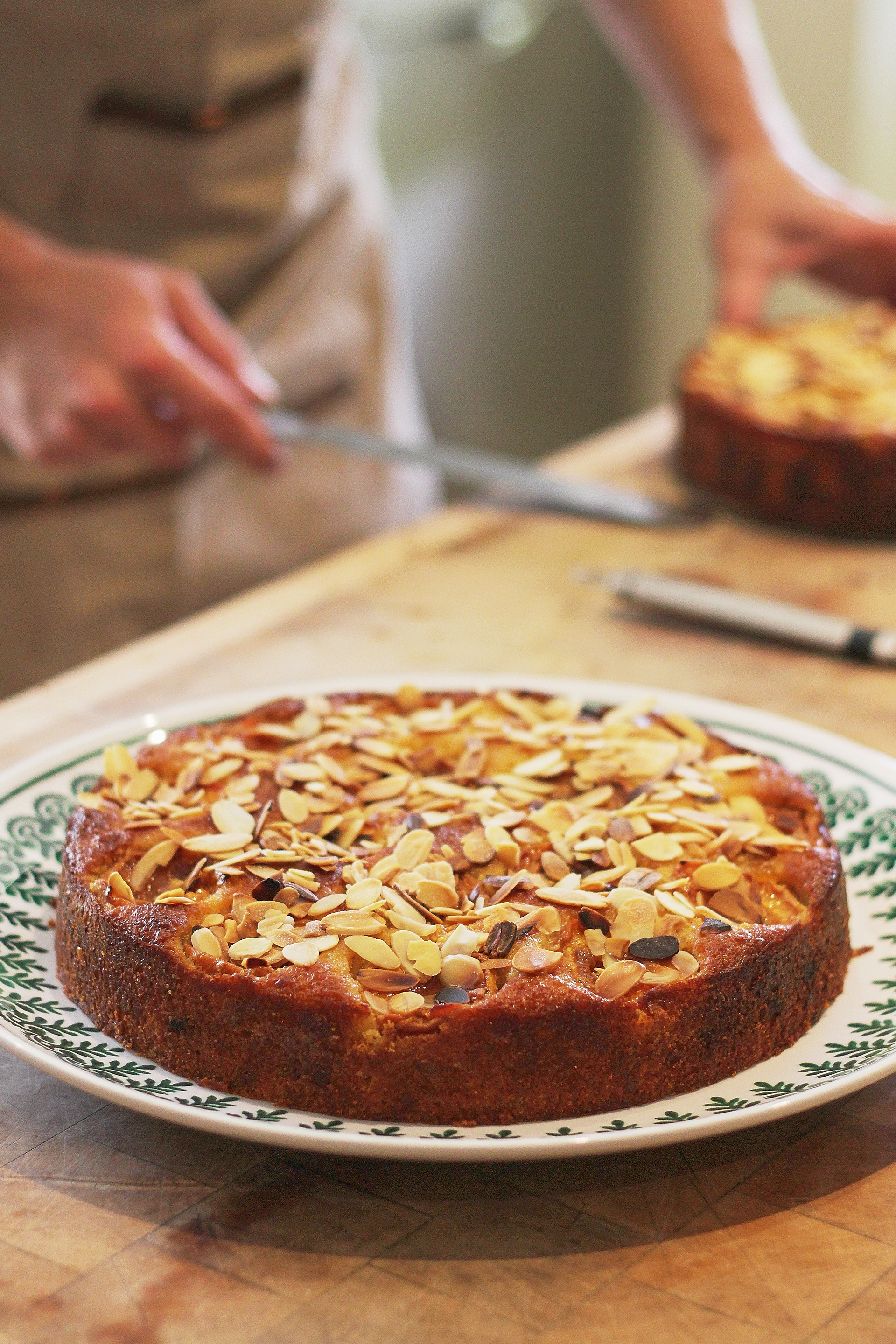 Person serving almond-topped cake on a plate at a table