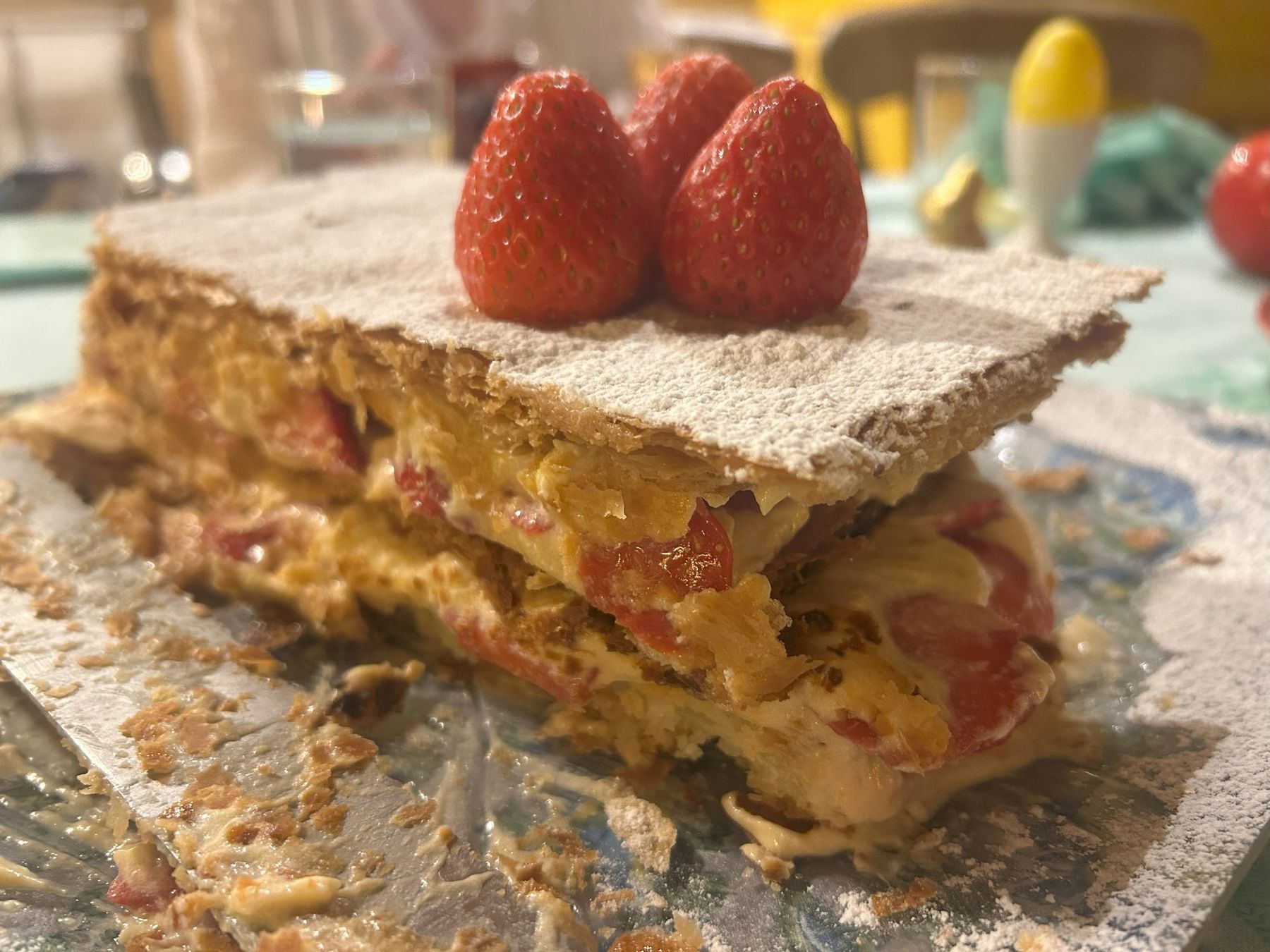 Powdered sugar pastry slice topped with two strawberries on a table