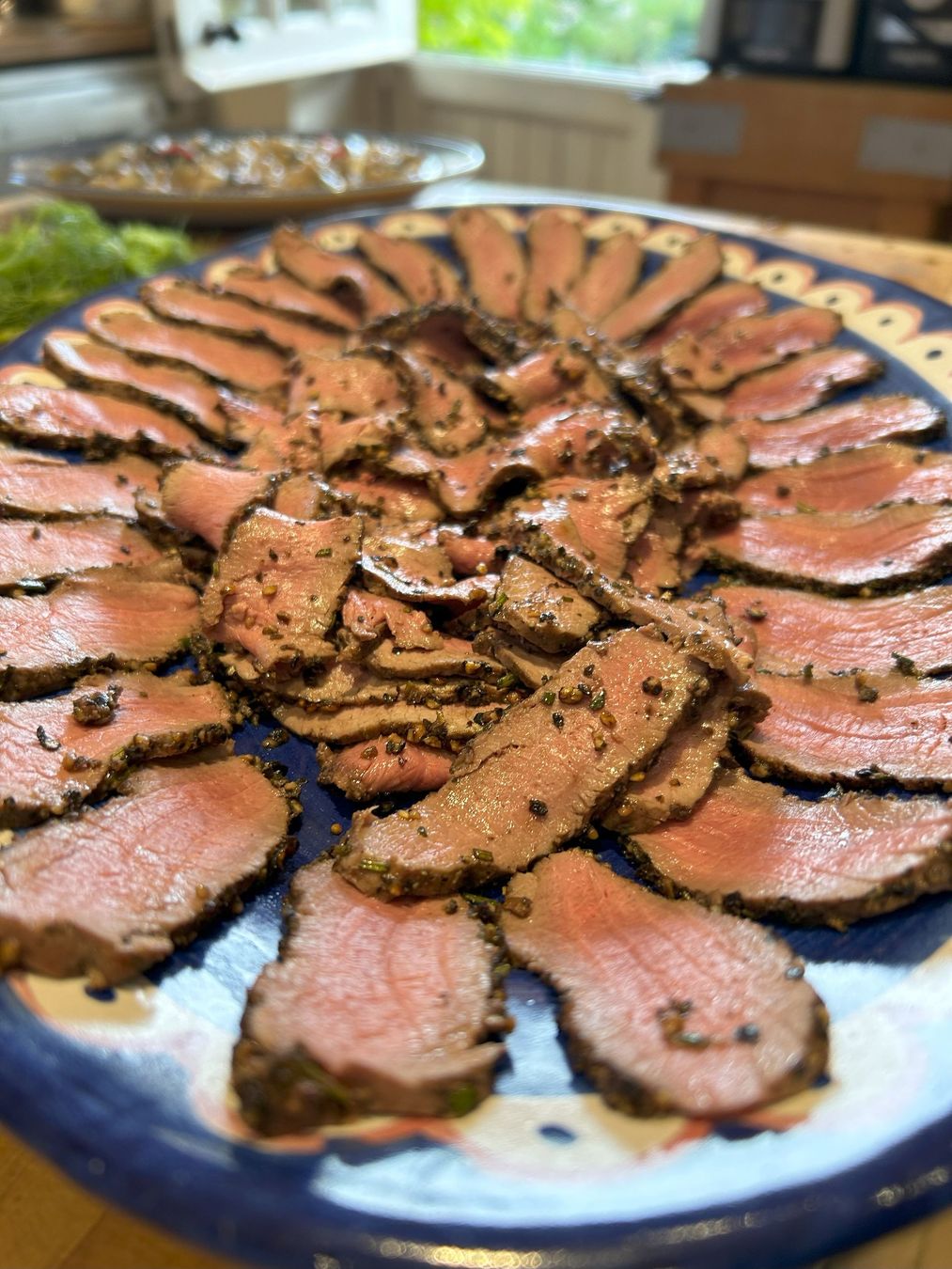 Sliced medium-rare roast beef arranged in a circular pattern on a blue platter, garnished with herbs.