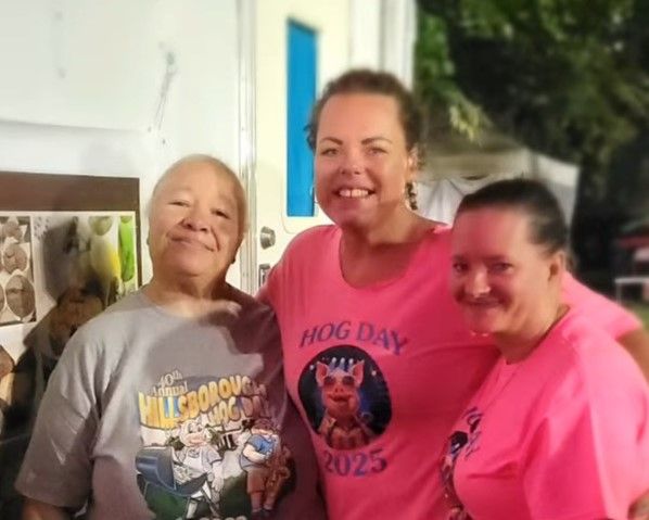 Three smiling people in pink shirts posing outdoors on a porch