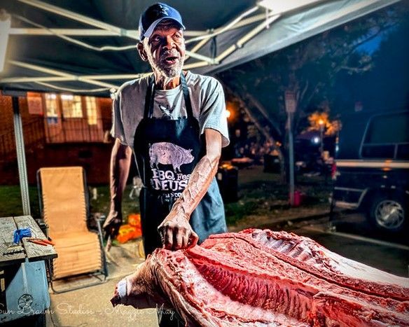 Butcher under a canopy carving a large slab of red meat at an outdoor market stall