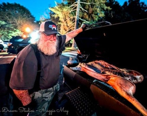 Man smiling beside an open smoker with whole fish grilling at night, lights glowing in the background