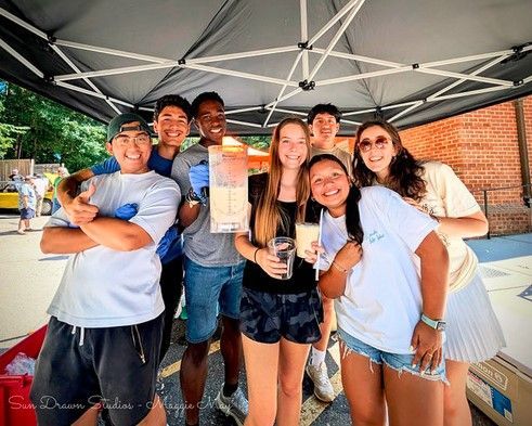 Group of friends smiling under a canopy, holding drinks at an outdoor event.