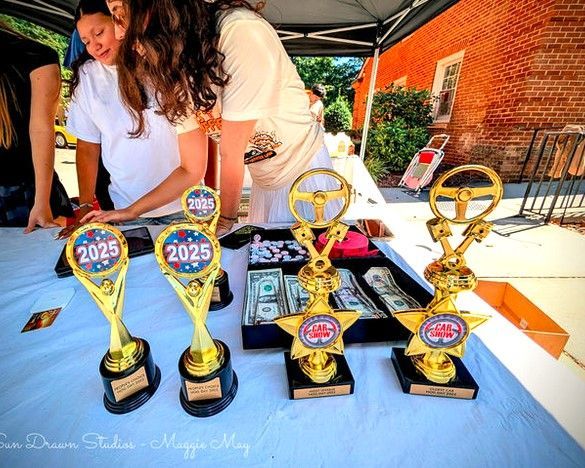 Trophy table with four gold awards and people arranging them under a canopy outdoors.
