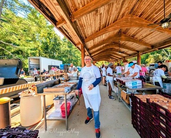 People serving food at an outdoor community meal under a wooden pavilion.