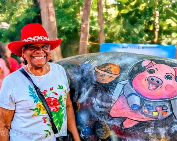 Smiling woman in red hat beside a painted cow sculpture outdoors