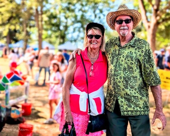 Couple smiling outdoors at a colorful festival, wearing bright green and pink clothing and sunglasses.