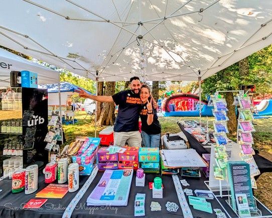 Booth under white canopy displaying colorful products, with two people smiling behind the table
