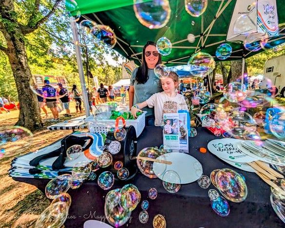Woman and child at an outdoor bubble festival under a green canopy, surrounded by colorful floating bubbles.