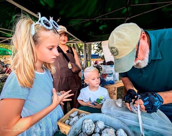 Vendor bagging rocks at an outdoor market while a child watches beside them.