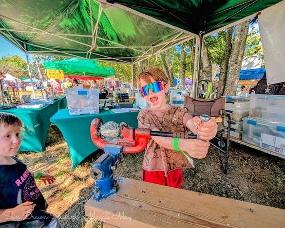 Two children at a colorful outdoor market stall with green canopy and toys on the table