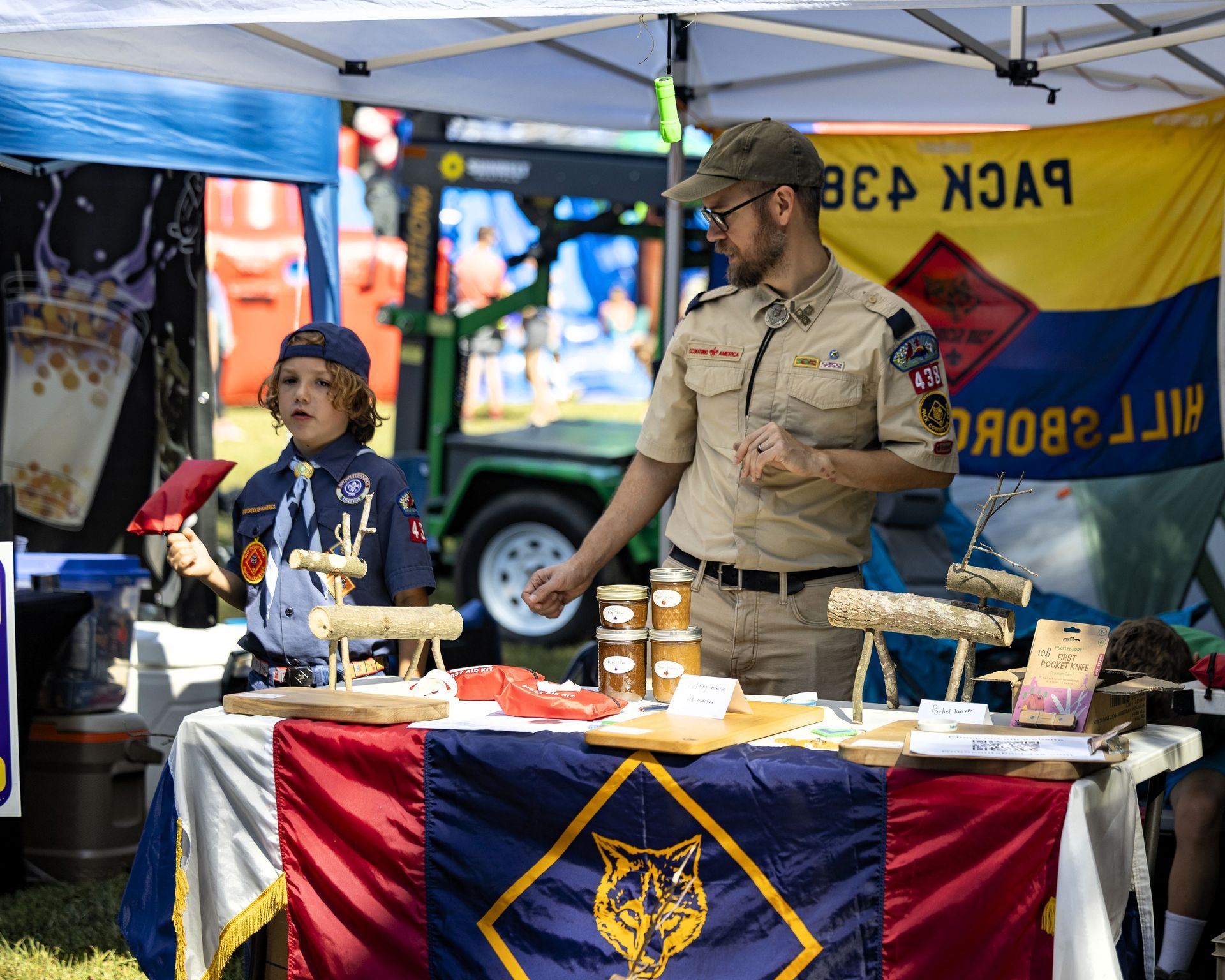 Two people at a booth displaying red, blue, and yellow flags and banners, with food and drinks on the table