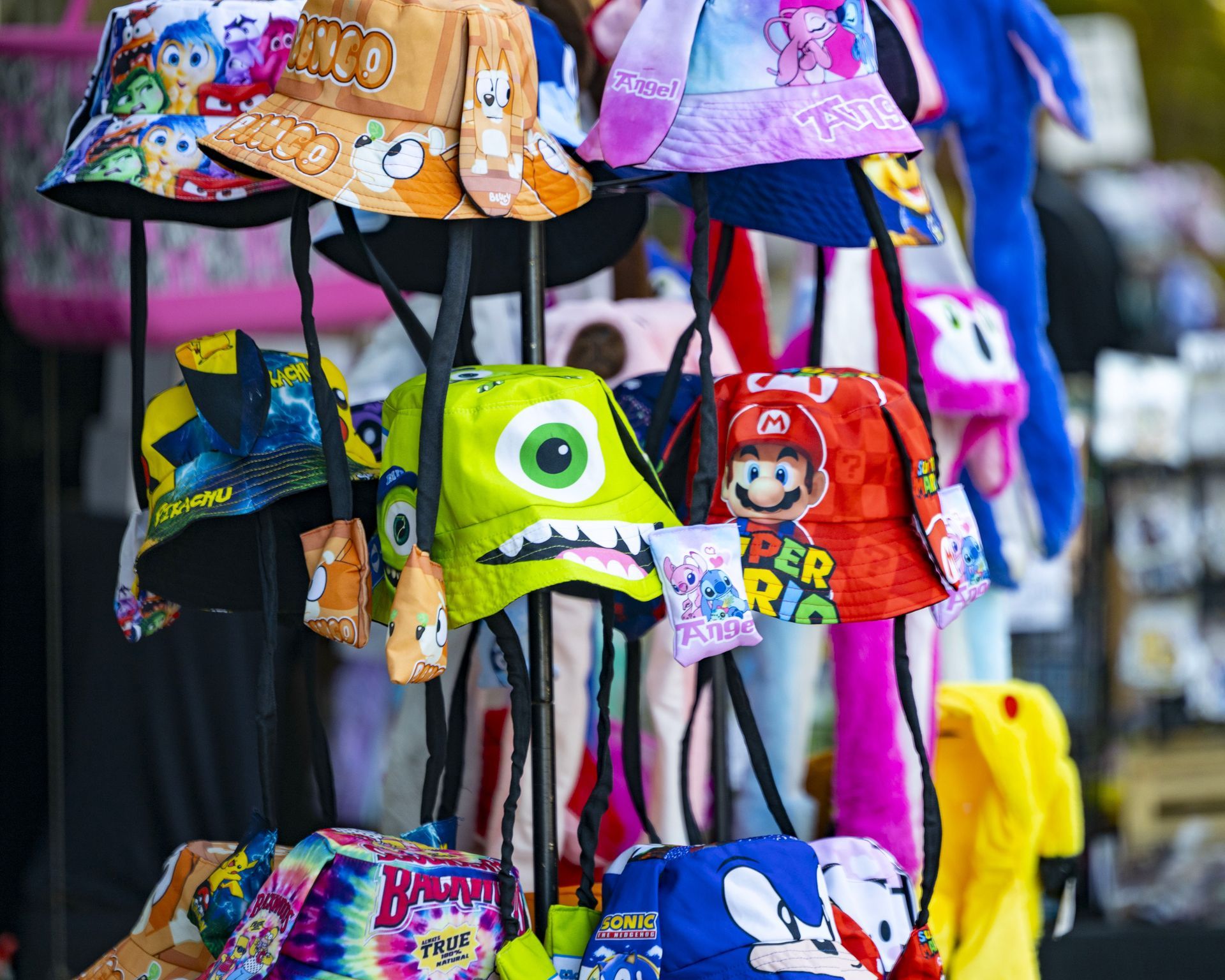 Colorful children’s bucket hats displayed on a rotating rack at an outdoor market.