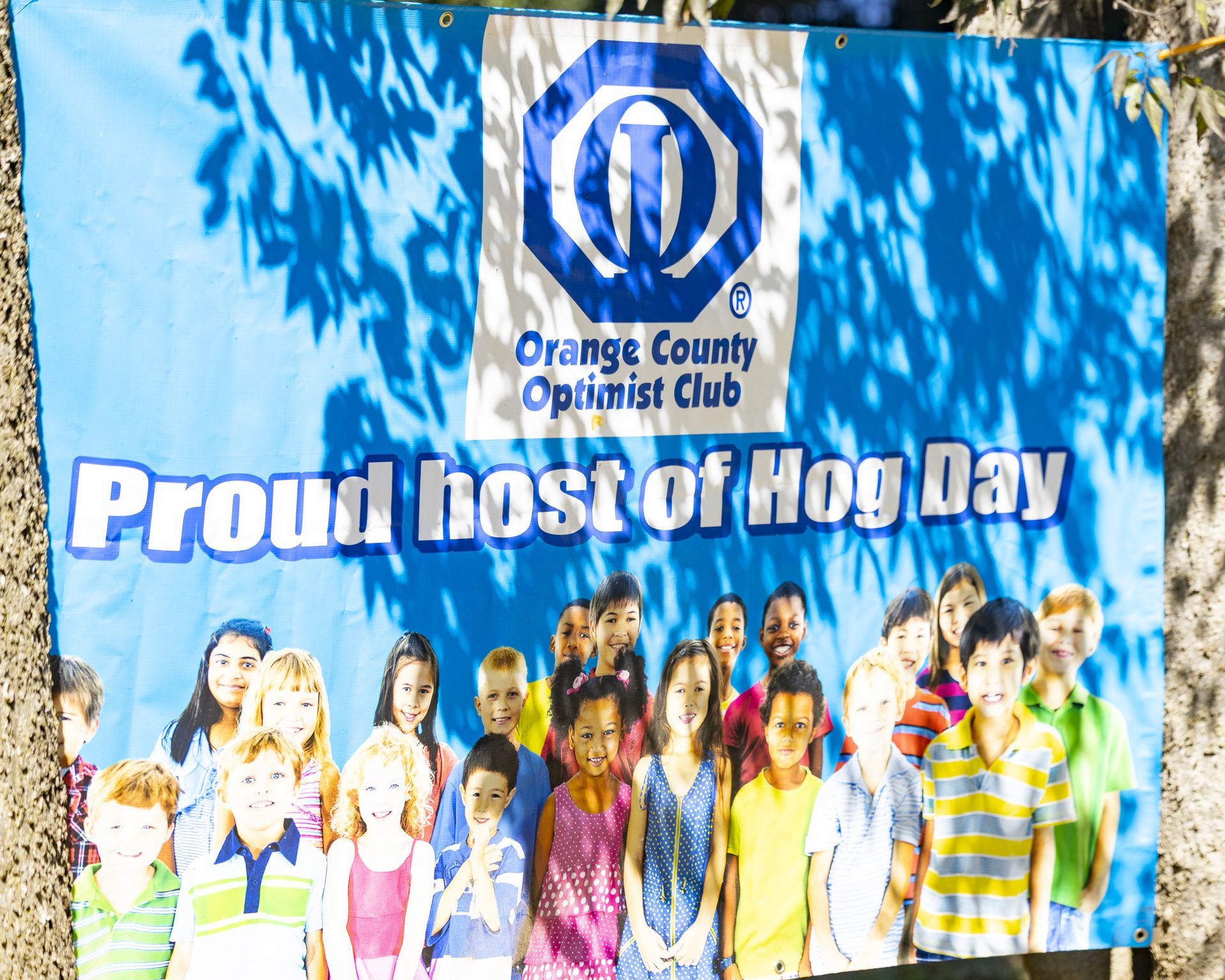 Orange County Optimist Club banner reading “Proud host of Hog Day” with a group photo against a blue background