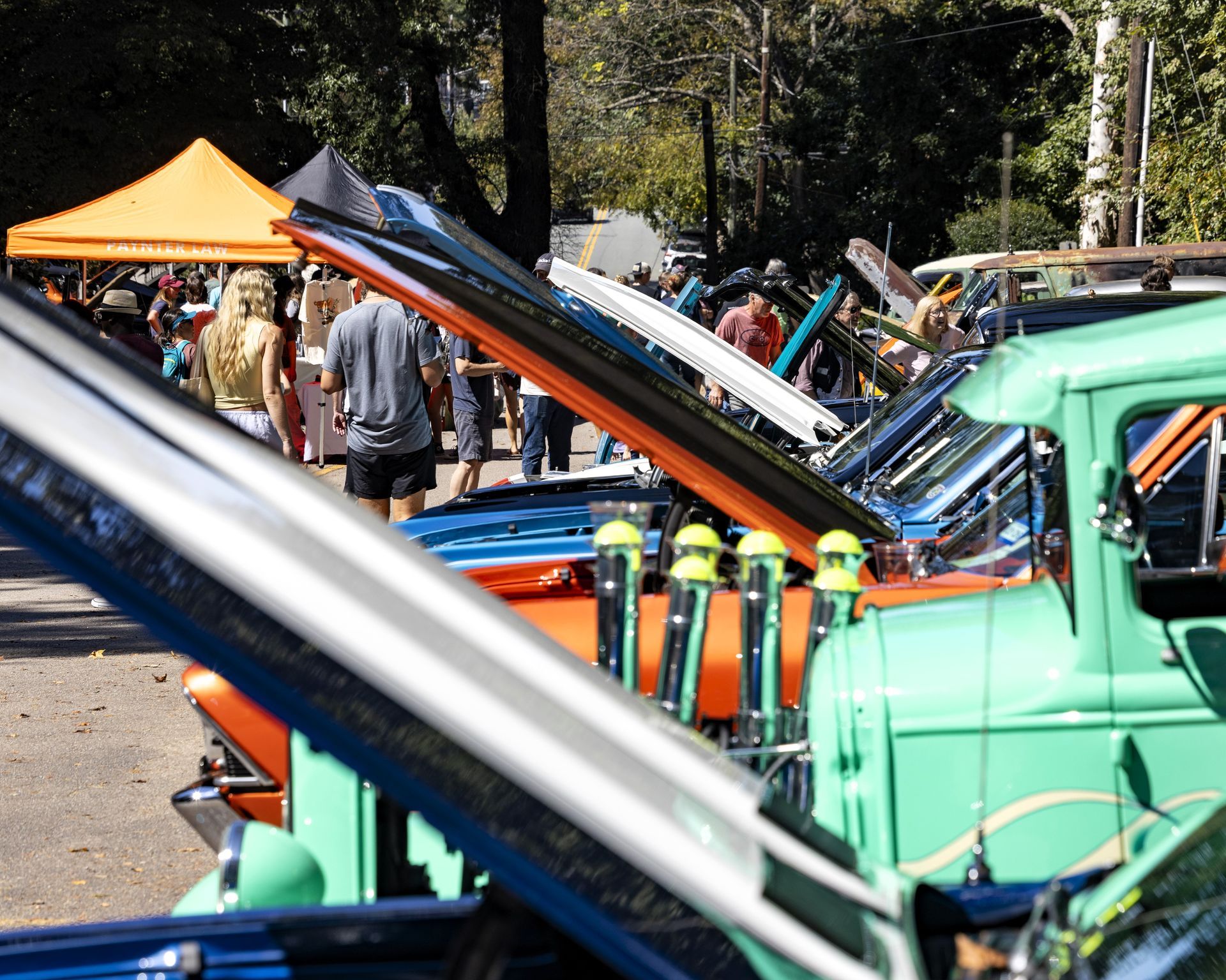 Classic cars with open hoods lined up at an outdoor car show, including a green truck in the foreground.