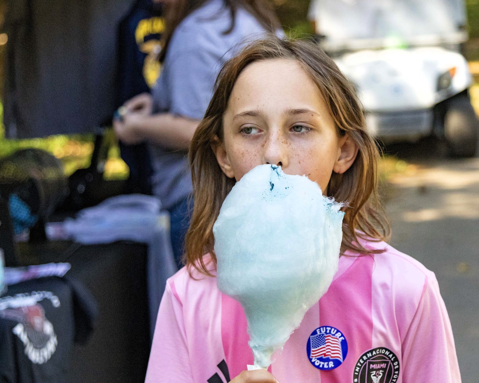 Child in pink shirt eating blue cotton candy at an outdoor event