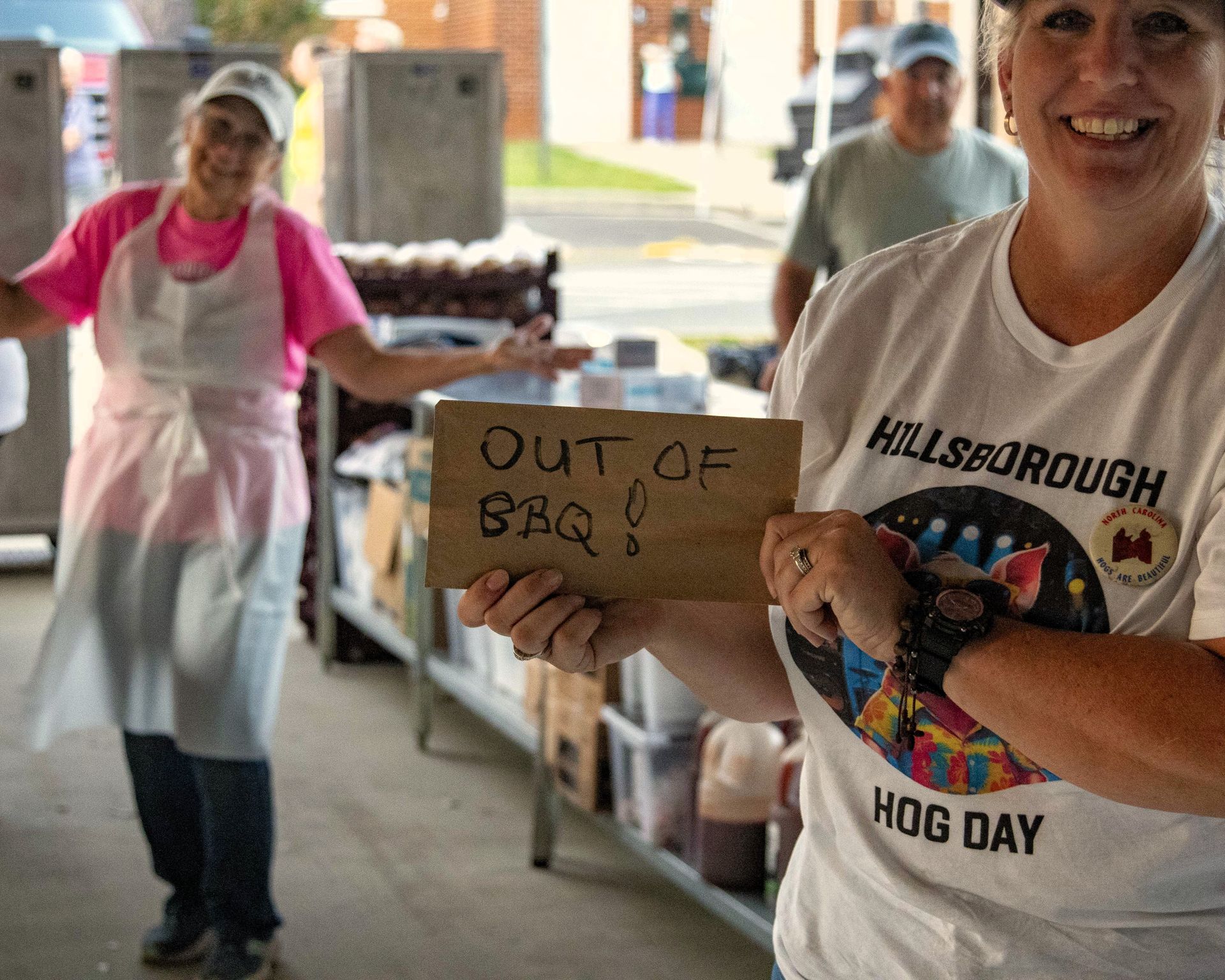 Woman in white T-shirt holding “Out of BBQ” sign at a Hillsborough Hog Day event.