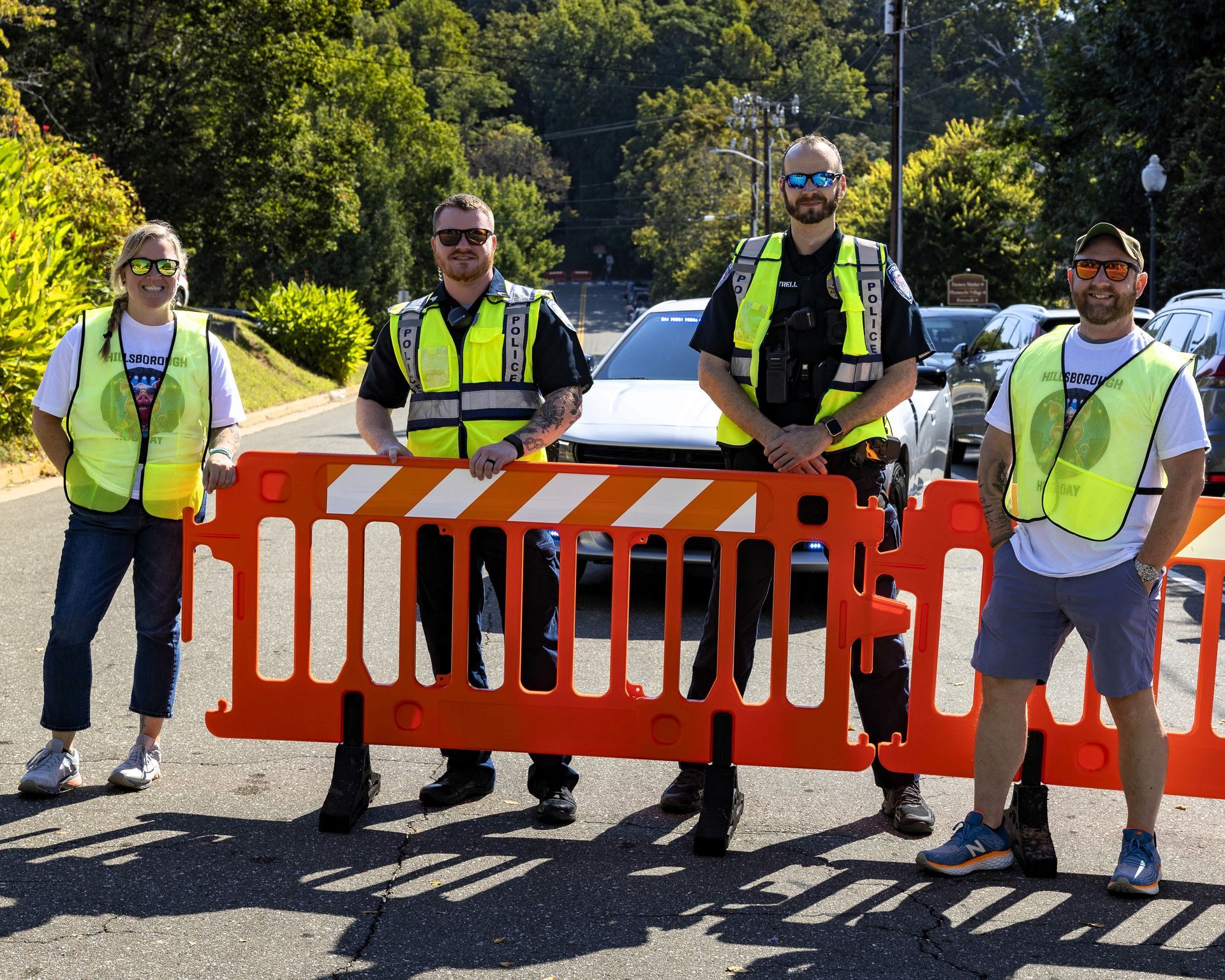 Four workers in neon vests hold an orange road barrier on a sunny street