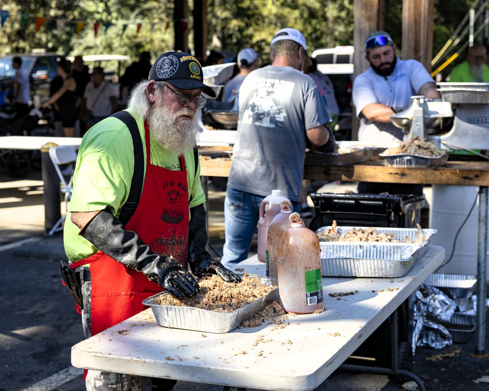 Volunteers serving food at an outdoor event, wearing aprons and gloves behind a buffet table