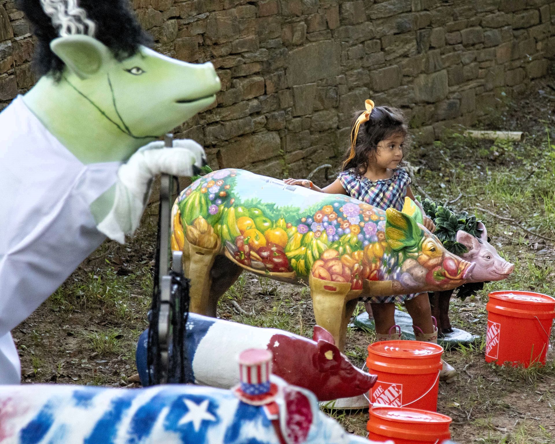 Colorful painted cows at a small outdoor display, with a child nearby and a person in a cow costume on the left