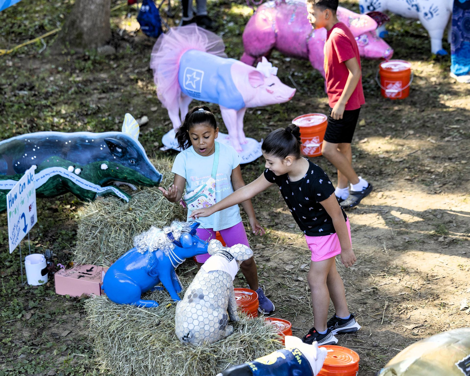 Children pet colorful painted animal figures outdoors on hay-covered ground