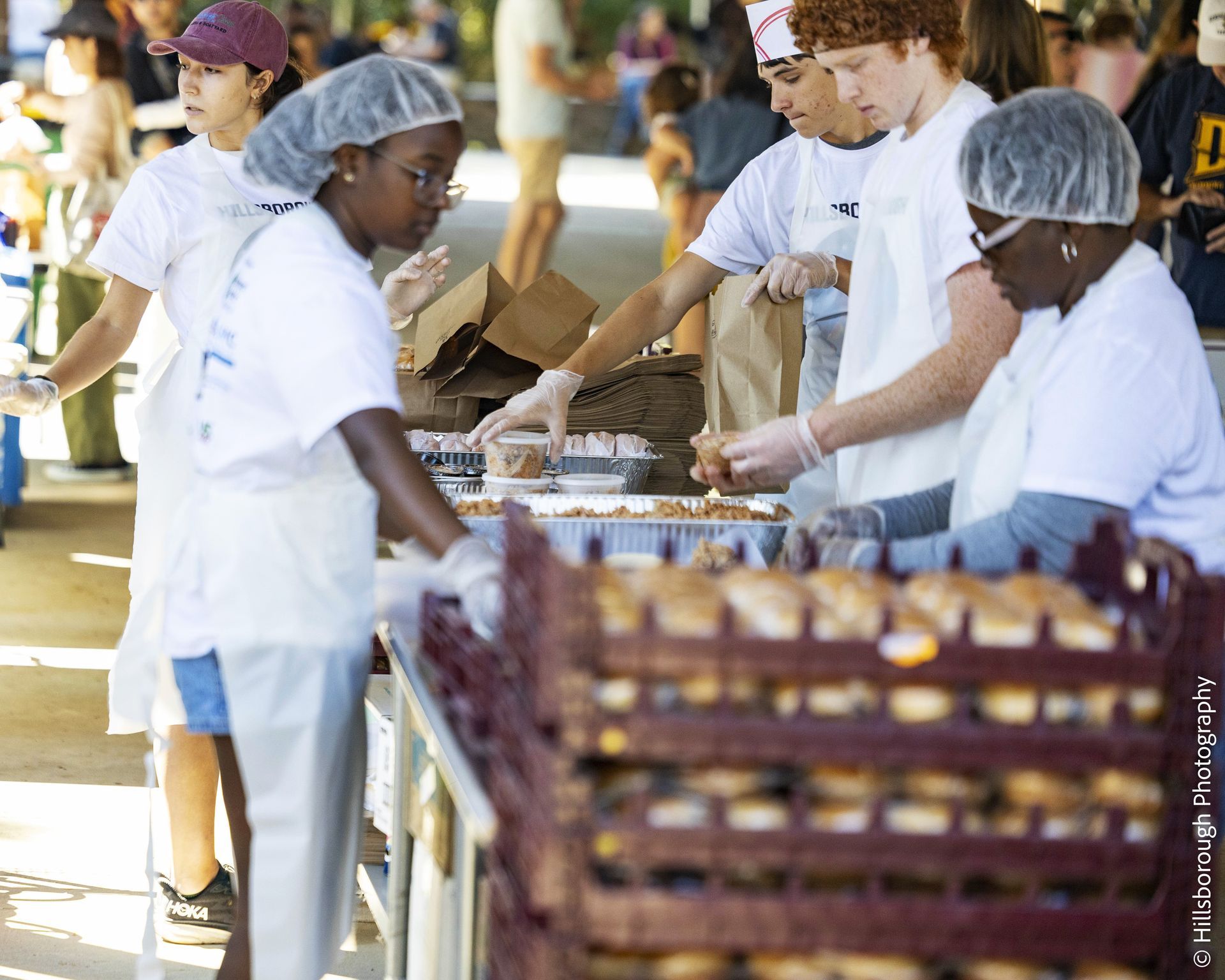 Volunteers in white uniforms sorting produce at an outdoor food distribution table