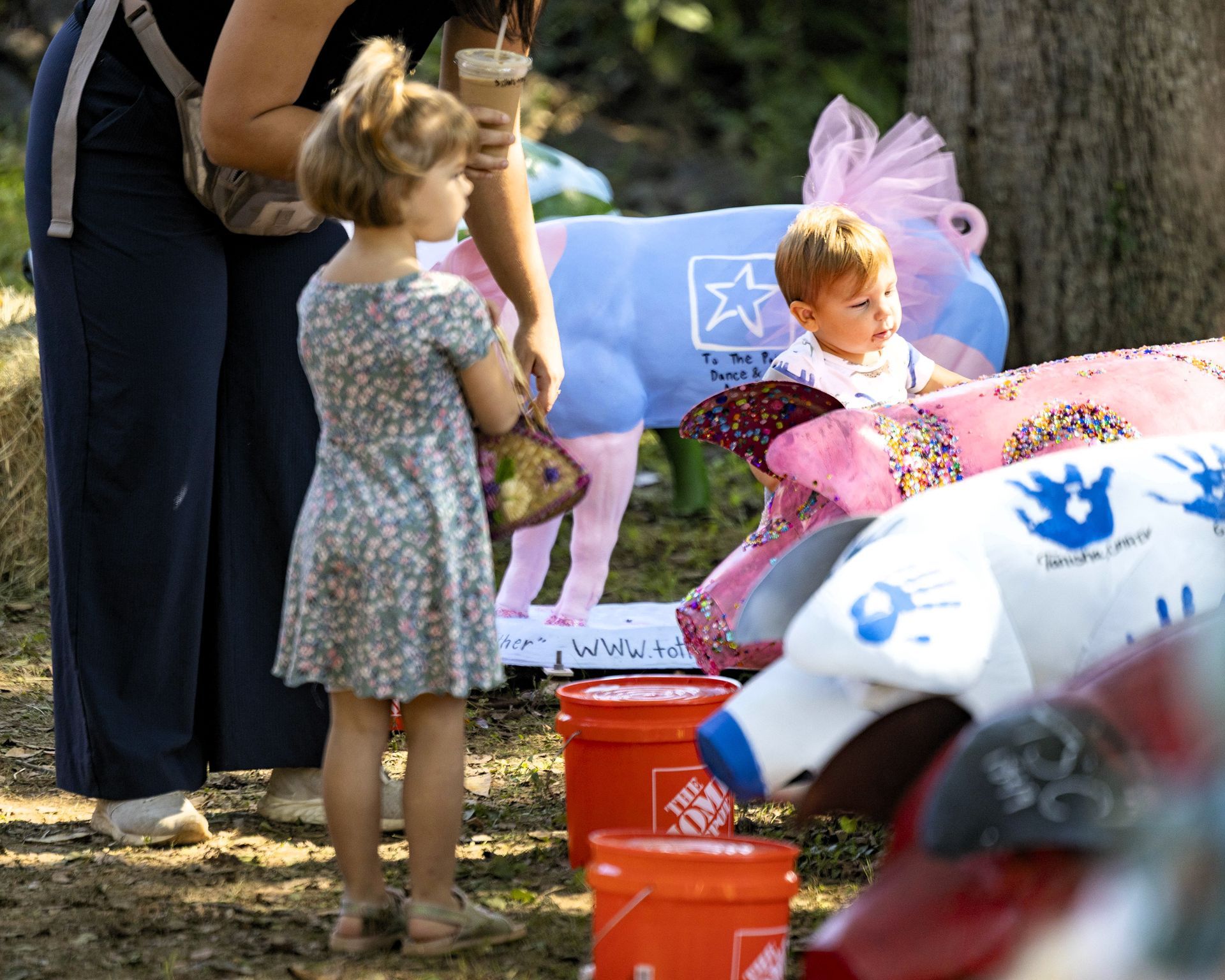 Children at a memorial with flowers, stuffed animals, and toy buckets outdoors