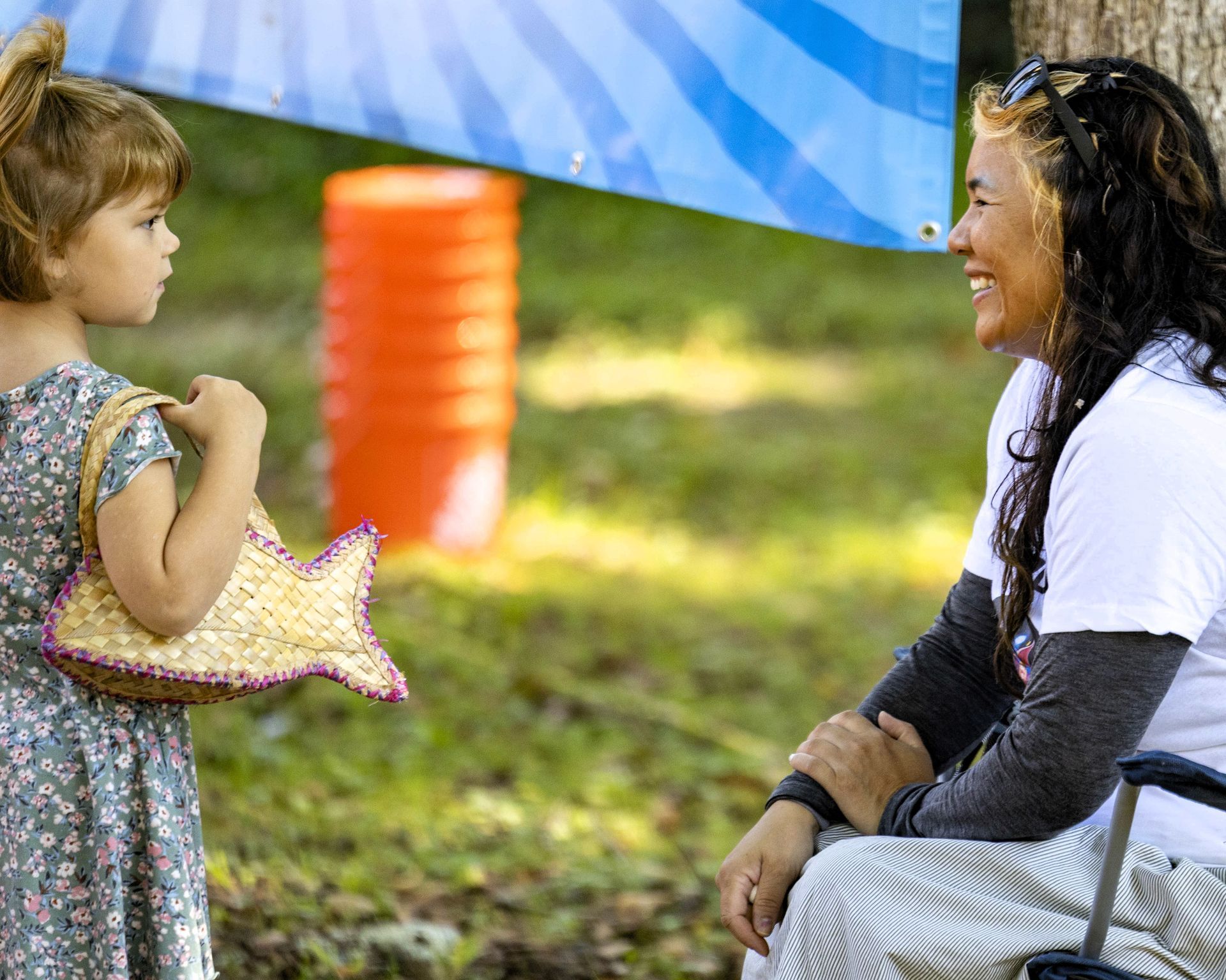 Child holding a star-shaped plush talks to a smiling woman outdoors under a blue canopy