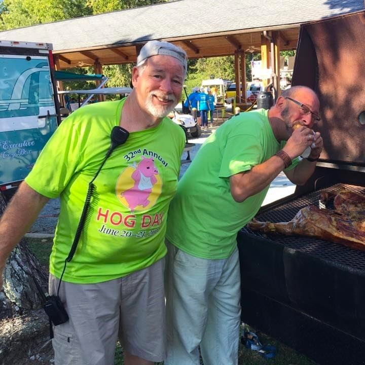 Two volunteers in bright green shirts serving food at an outdoor event under a pavilion