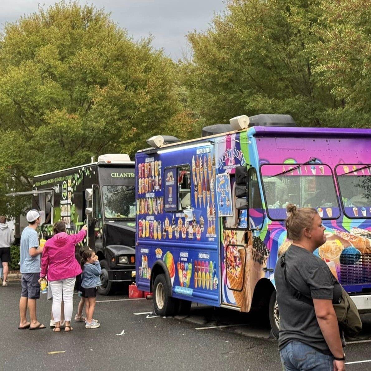 Colorful ice cream truck at a park event with people lined up nearby