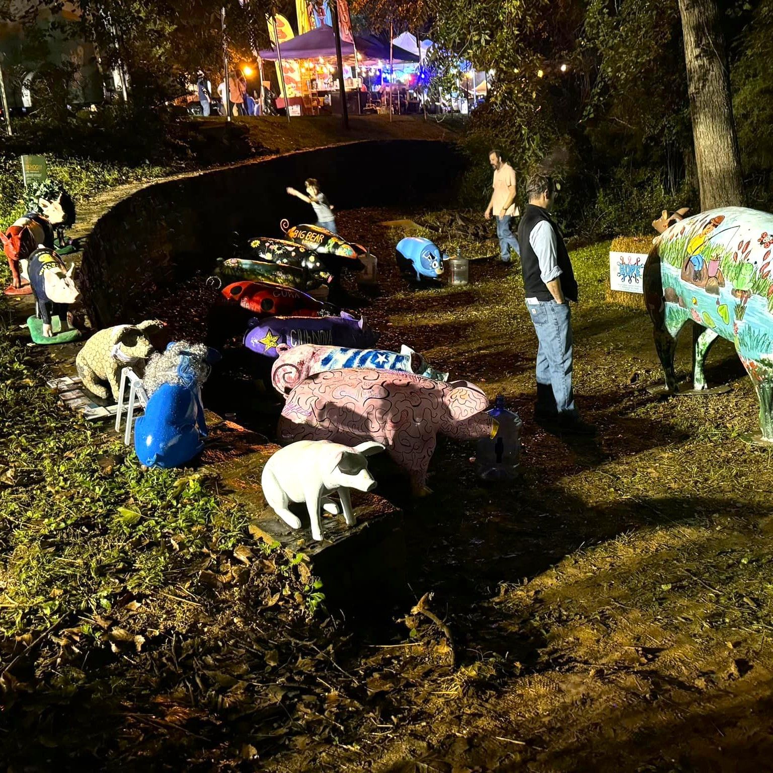 People in colorful pig costumes gathered outdoors at night around a muddy trench.
