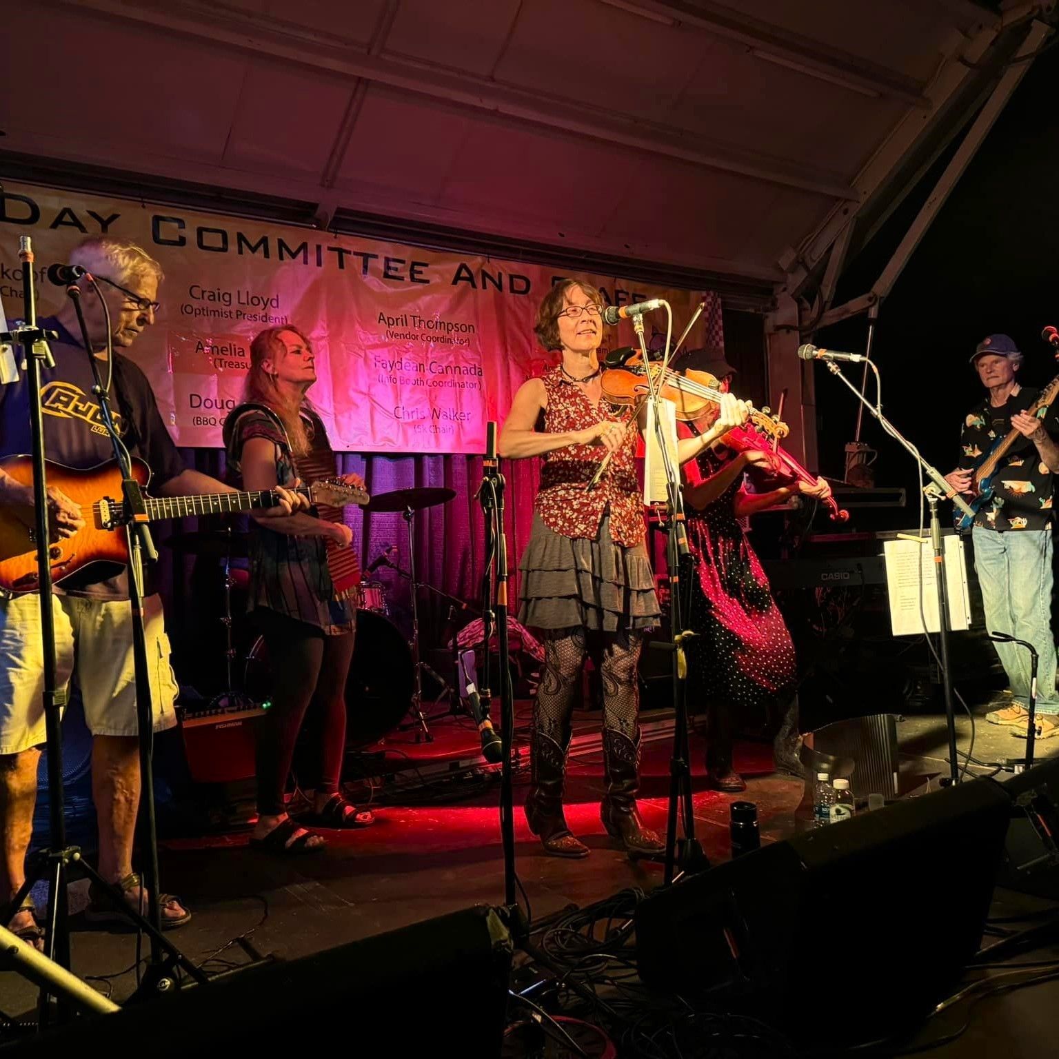 Live band performing on a dimly lit stage with red lighting and multiple musicians at microphones and instruments